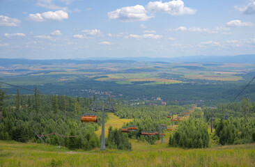 Elevated view of chairlifts descending a forested hillside with expansive farmland and villages in the distance.