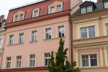 A charming pink building featuring a striking red roof along with a vibrant tree positioned nicely in front of it, creating an attractive scene