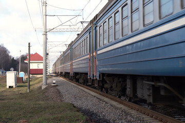 A blue train speeds past a quaint station set in a rural landscape
