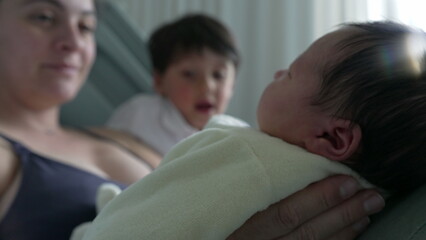 Mother and older sibling cuddling close to newborn baby, smiling warmly. intimate family moment...
