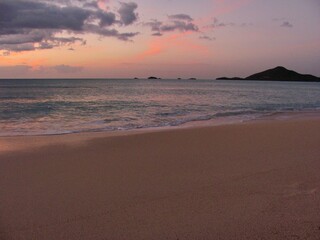 A tranquil beach scene featuring colourful skies reflecting off the gentle ocean waves during dusk.