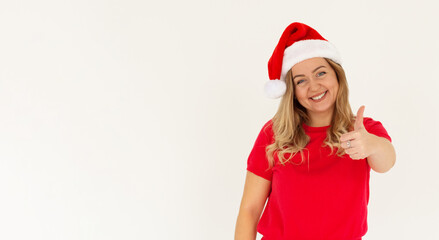 Young funny european woman in red t-shirt and christmas hat showing thumb up and smiling. Happy New Year and Merry Christmas concept