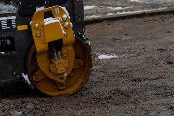 Close-up view of orange road roller compacting brown dirty ground in a cloudy winter day. Some snow on ground. Soft focus. Copy space. Road construction machinery theme.