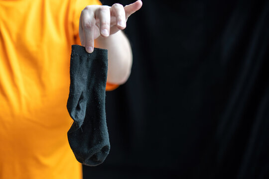 hand distastefully gripping a black sock against a dark background, embodying themes of disgust and neglect. It invites reflection on cleanliness and human habits