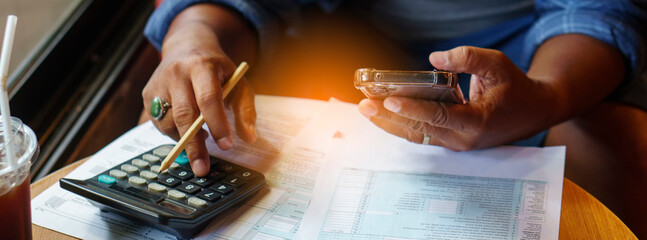 Business man use calculator, smartphone, and review tax form at home office. Financial advisor hand plan and calculate budget. Business and Financial Planning Concept-banner image.