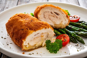Cutlet de Volaille, wrapped chicken cutlet served with cooked green asparagus on wooden table