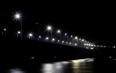 Bridge at night with lit street lamps, from the river bank. Urban night landscape, with defocused...