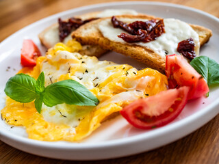 Continental breakfast - scrambled eggs, bruschetta and fresh vegetables on wooden table