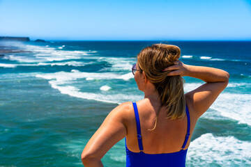 Beautiful mature woman in swimsuit standing and looking at ocean in Portugal. Back view