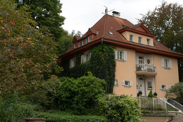 An expansive and large house featuring a vibrant red roof is beautifully surrounded by an abundance of lush trees and vibrant bushes
