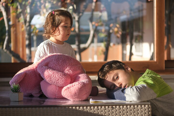 Little girl tries to play with her brother. The siblings spend time together with a pink teddy bear.