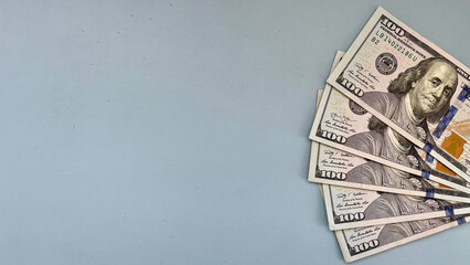 Fan of 100 US dollar bills on a blue background, offering abundant copy space. Ideal for financial advertisements, banking services, or wealth-related content.