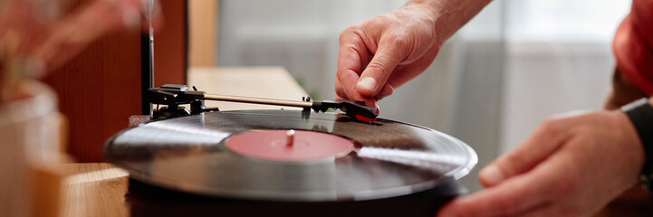 Side view closeup of unrecognizable senior man carefully setting up retro record player at home and...