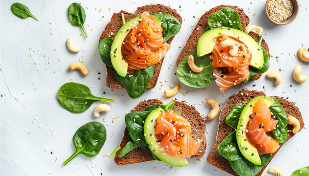 Plate of four sandwiches with avocado and salmon on top. The sandwiches are served on a white background