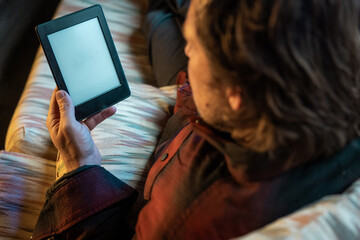 A man is sitting on a couch reading an e-book. He is smiling and he is enjoying himself