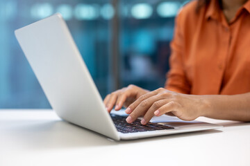 Hands typing on laptop in office. Business professional in orange shirt working efficiently....