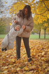 Little boy playing in autumn park. Child on yellow fallen leaves on a sunny autumn day.