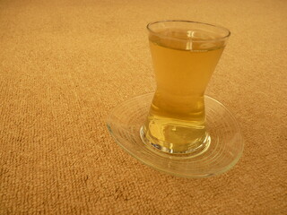 A glass of nettle tea symbolizing natural healing and warmth, served in a traditional glass, placed on a soft beige surface, evoking a sense of calm, connection to nature, and the simplicity of herbal