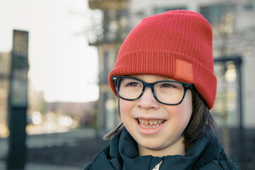 Smiling Child With Glasses Wearing a Red Hat in Urban Setting