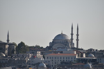 Obraz premium View of a mosque with its iconic dome and minarets rising above the cityscape of Istanbul, surrounded by buildings under a hazy sky 