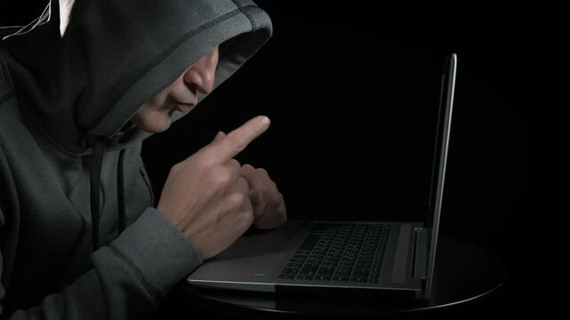 Pensive hacker in front of screen. A pensive freelancer hacking on his notebook against black background.