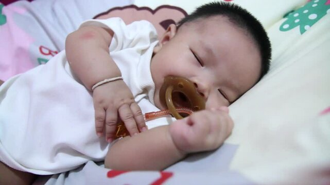 Baby is sleeping while sucking on a pacifier.
