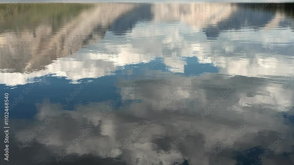 Wall mural reflection of a mountain, blue sky and clouds in a calm lake with small ripples