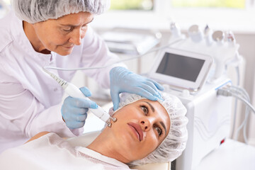 Obraz premium Young female client receiving hardware ultrasonic to revitalize and tighten facial skin at cosmetology clinic