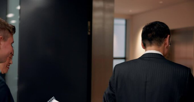 People, business and walking to elevator in office for meeting, lunch break and polite greeting. Lawyers, coworkers or lift in Japanese law firm for teamwork, corporate mediation or diversity at back