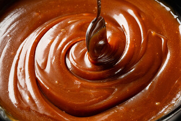 Cooking caramel sauce, mixing  with a spoon, close up, food background.