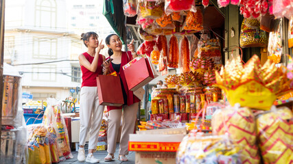 Fototapeta premium Happy Asian family celebration Chinese lunar new year festival together. Mother and daughter in red blouse holding shopping bag walking and buying home decorative ornaments at Chinatown street market.