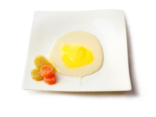 Condensed milk and custard desert looks like a fired egg and colorful jelly sweets in sugar on a white fancy square plate and light background. Creative food ideas. Light and airy look