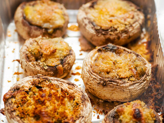 Cooked high quality stuffed mushrooms in a foil tray on wooden board and table. Fine starter dish with premium ingredients .