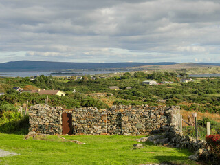 Remains of an old stone building, green grass field and ocean and mountains in the background....