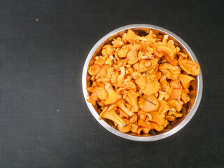 Metal stainless bowl full with fine golden chanterelle mushrooms on dark mesh surface. Tasty nature product collected in clean forest for cooking. Fine organic food.