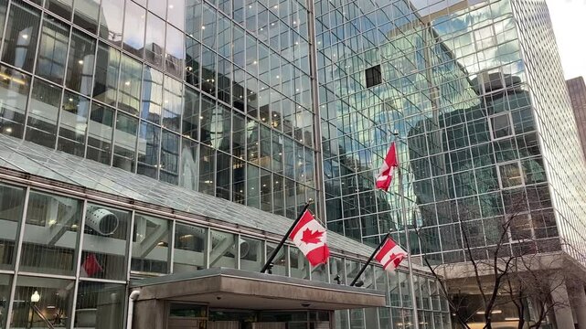 Three Canadian flags waving in front of a modern glass building in downtown Ottawa, reflecting the city's urban landscape and national pride