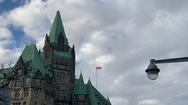 Canadian flag waving atop a historic building in Ottawa, showcasing a blend of architectural heritage and national pride under a partly cloudy sky.
