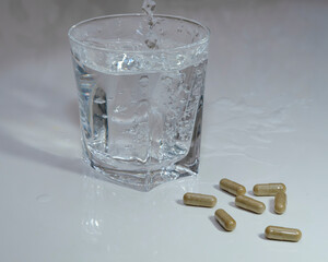 medicinal capsules lie next to a glass transparent glass into which water is poured on a white background