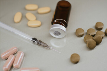 A syringe with a thin sharp needle, an injection ampoule and multi-colored pills