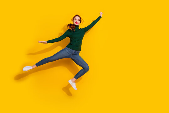 Full length photo of adorable lovely girl wear green pullover jumping high risig fist empty space isolated yellow color background