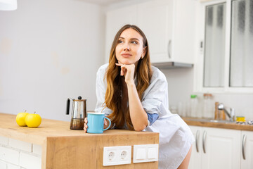 Portrait of smiling young woman drinking morning coffee at home kitchen