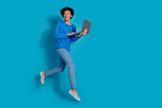Full body photo of attractive young man running hold netbook dressed stylish clothes isolated on blue color background