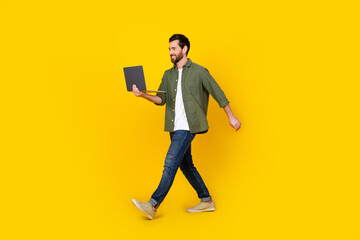 Full length portrait of nice young man walk use laptop wear shirt isolated on yellow color...
