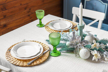 A beautifully arranged Christmas holiday table features green glass goblets, stylish plates, and a festive centerpiece. The cozy dining area is decorated with seasonal elements and a calm ambiance.