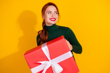 Fototapeta premium Photo of charming positive woman wear green turtleneck holding present box empty space isolated yellow color background