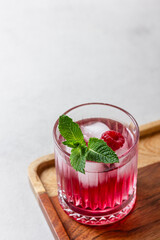 Raspberry cocktail with ice in a glass on a light background