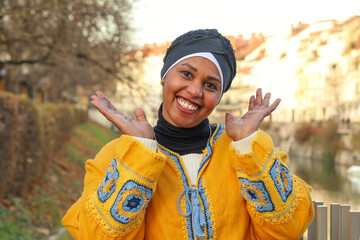 Black woman with dimples in ethnic yellow boho style clothes smiling charmingly in park with arms...