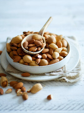 A white bowl full of shelled and unshelled almonds on a white wooden background