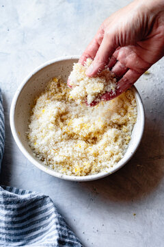 A hand rubbing lemon zest into a bowl of sugar