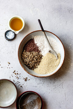 An assortment of seeds and flour in a bowl, accompanied by oil and salt, set against a textured background.